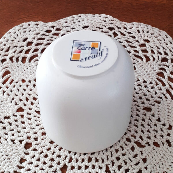 On voit le logo Mon carré créatif sous le pot de bougie fait main qui est posé à l'envers sur un napperon d'un buffet en bois rustique.