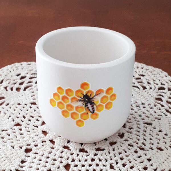 Pot de bougie fait main, posé sur un buffet en bois et napperon. Illustration abeille sur alvéoles - Mon carré créatif